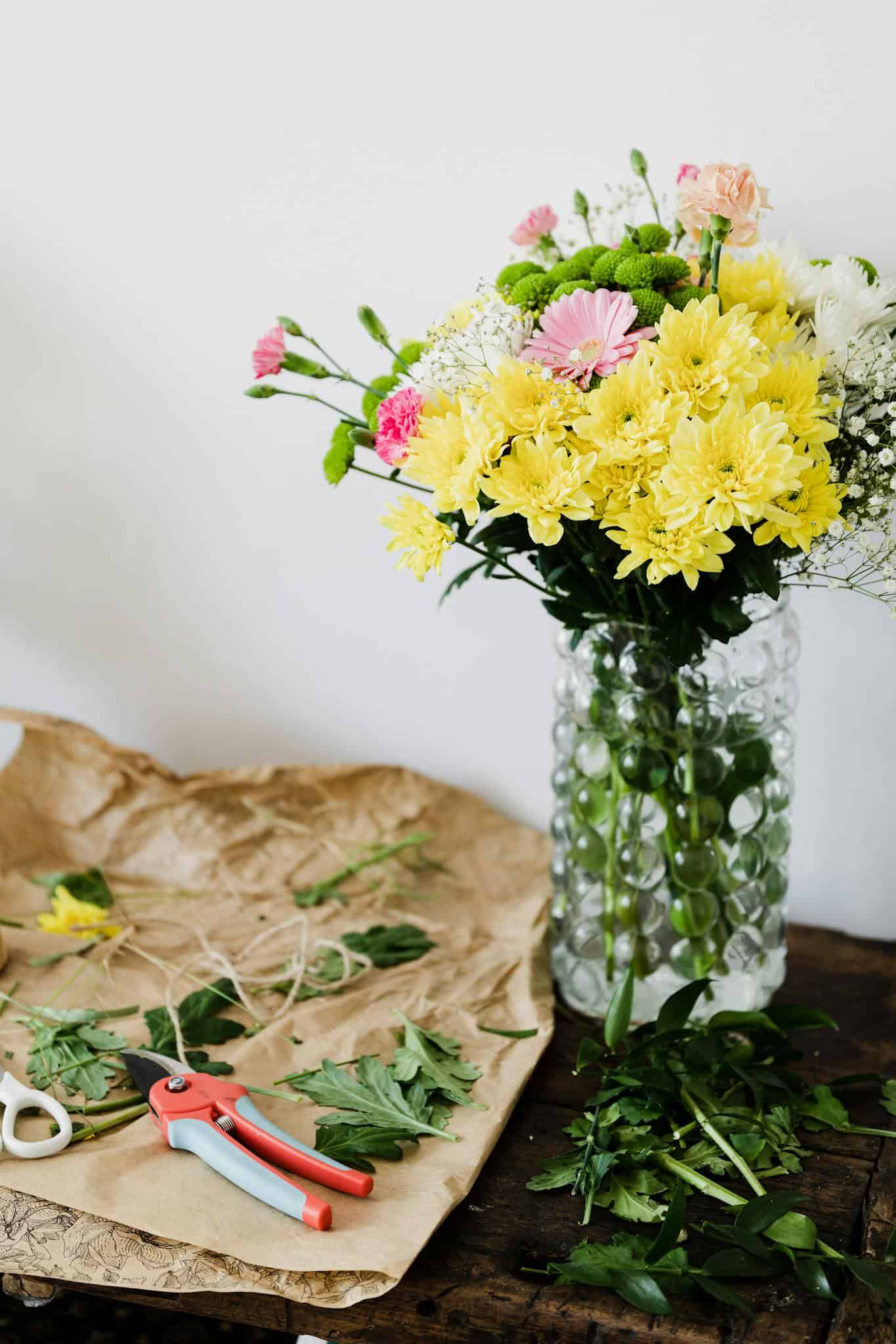A colorful bouquet of mixed flowers with tools for arranging on a wooden table, embodying creativity.